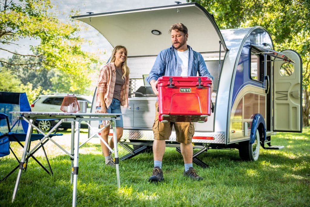 man loading cool out of clamshell camper rear kitchen storage